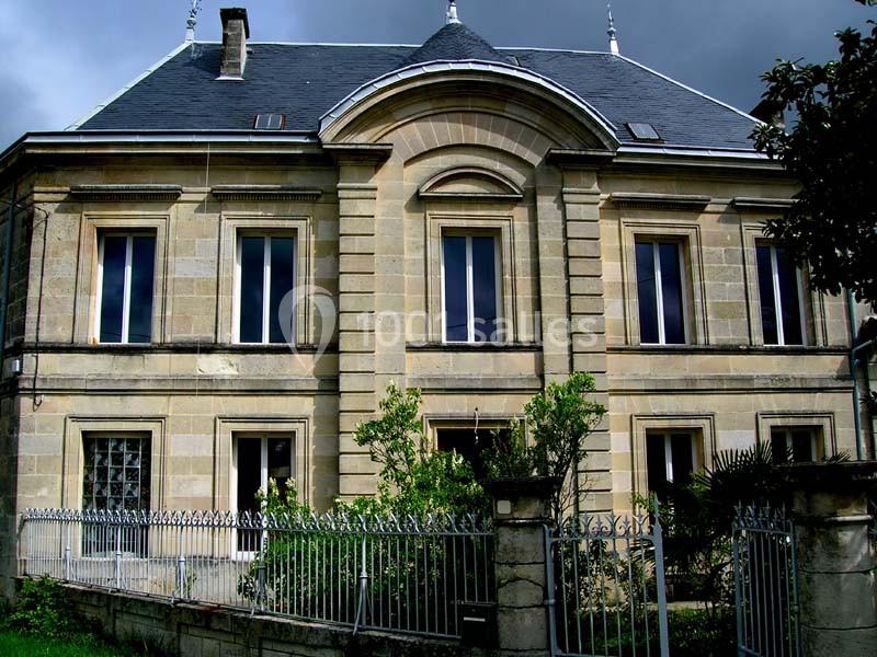 Façade d'une maison en pierre avec toit en ardoise, fenêtres symétriques et jardin clôturé au premier plan.