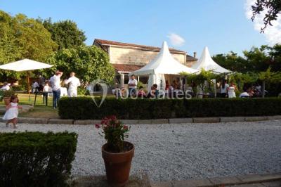 Façade d'une maison en pierre avec toit en ardoise, fenêtres symétriques et jardin clôturé au premier plan.