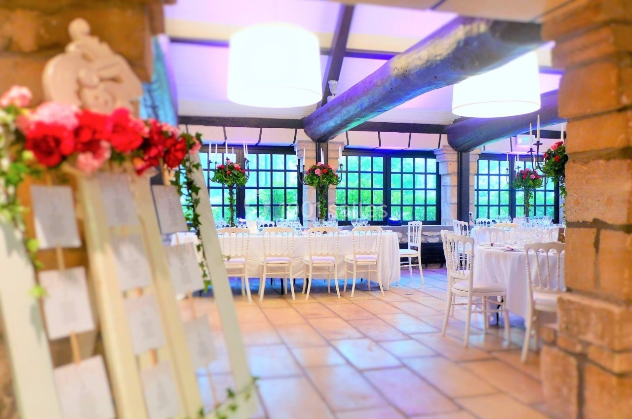Salle de réception lumineuse avec tables décorées, chaises blanches et arrangements floraux rouges.