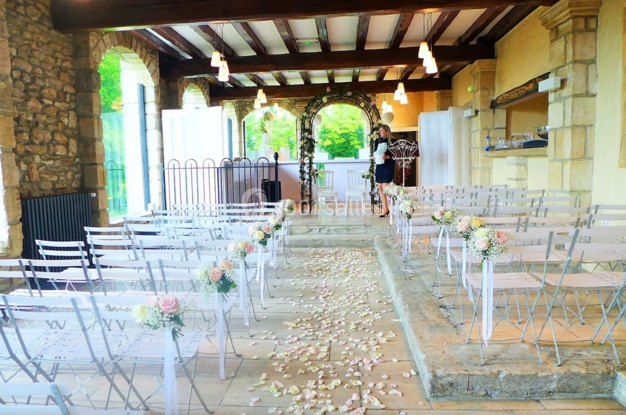 Salle de cérémonie décorée avec des chaises blanches, pétales au sol et fleurs sur les allées, prête pour un mariage.