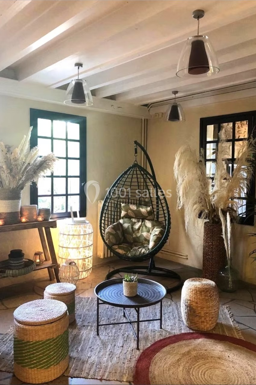 Espace intérieur chaleureux avec fauteuil suspendu, décorations en osier, plantes séchées et lumière naturelle.
