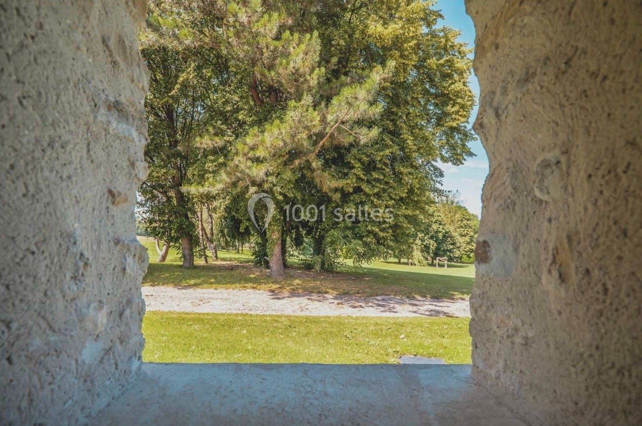 Vue sur un parc verdoyant avec des arbres, encadrée par une ouverture en pierre.