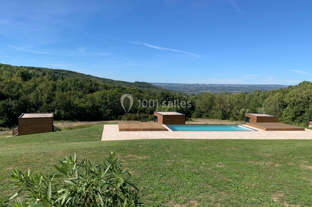 Piscine extérieure entourée de pelouse, avec vue sur des collines boisées sous un ciel bleu dégagé.
