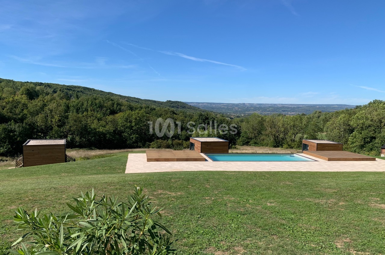 Piscine extérieure entourée de pelouse, avec vue sur des collines boisées sous un ciel bleu dégagé.
