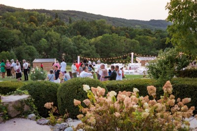 Tentes blanches pointues installées dans un jardin paysager avec vue sur une vallée boisée sous un ciel partiellement…