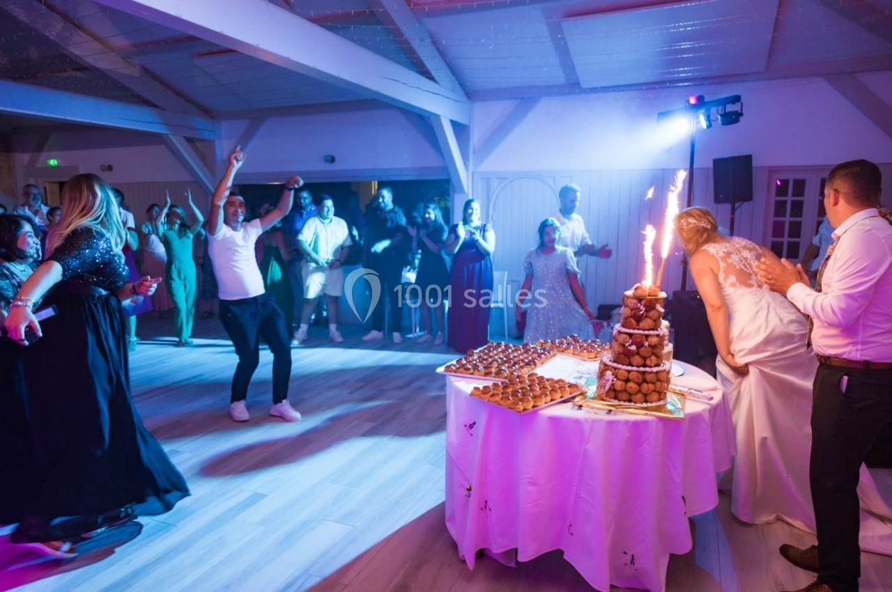 Des invités dansent autour d'une pièce montée éclairée par des cierges magiques lors d'une fête en salle.