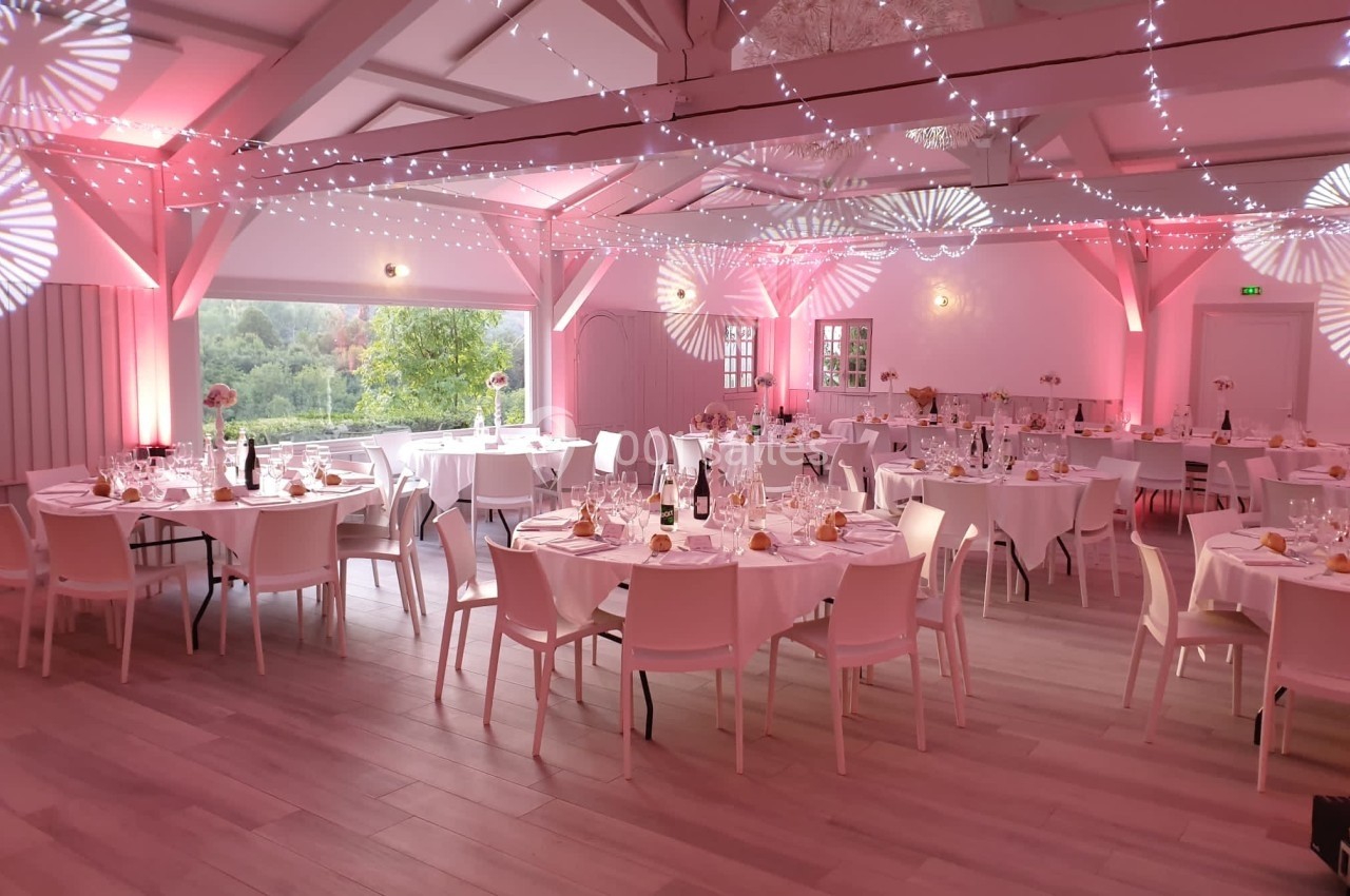 Salle de réception décorée avec des tables dressées, éclairage rose et guirlandes lumineuses suspendues.