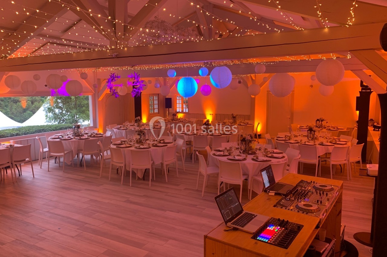 Salle de réception décorée avec des guirlandes lumineuses, des lanternes suspendues et des tables dressées pour un événement.