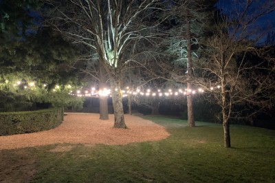Tentes blanches pointues installées dans un jardin paysager avec vue sur une vallée boisée sous un ciel partiellement…