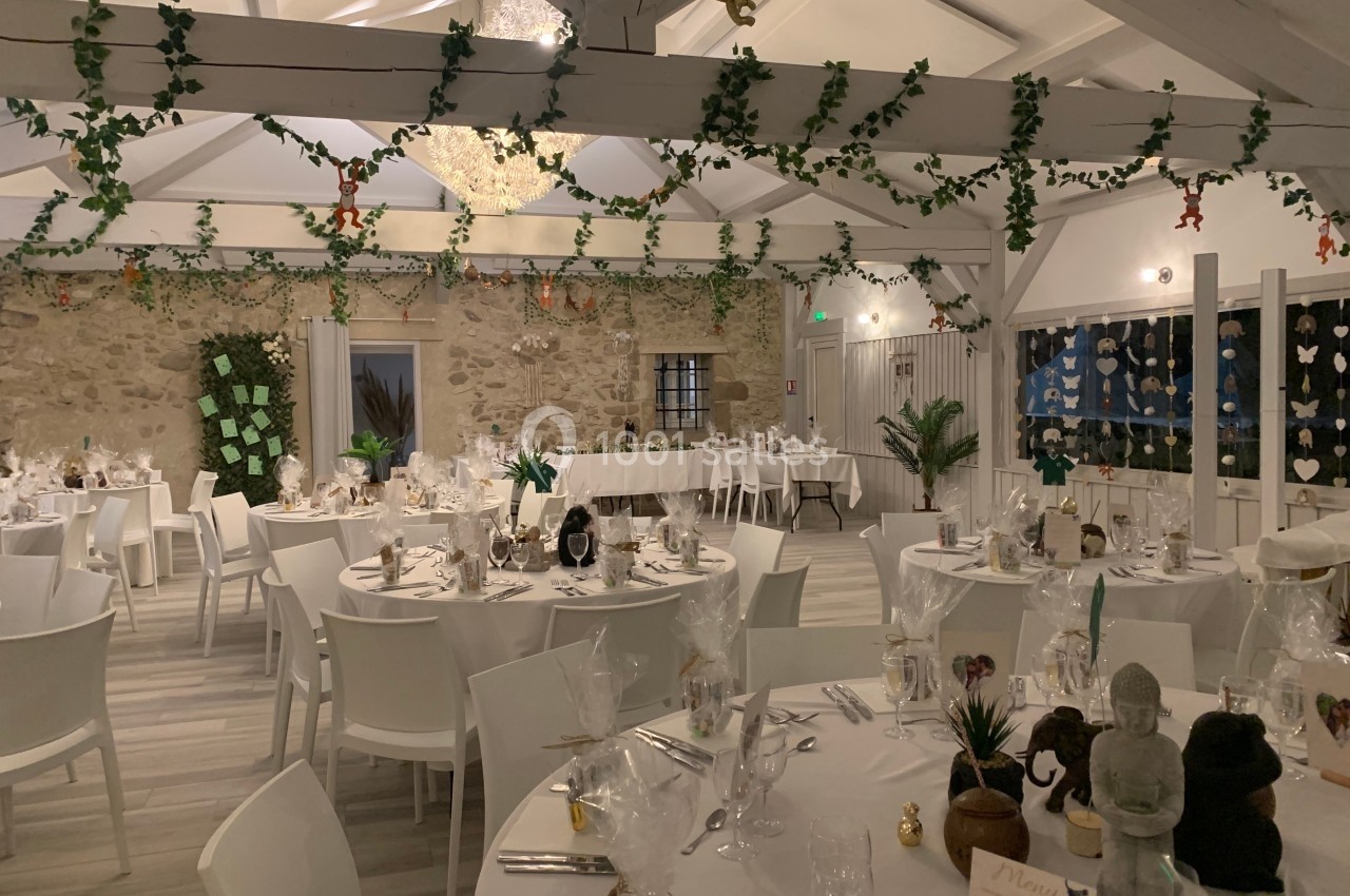 Salle de réception décorée avec des tables rondes dressées, des guirlandes végétales et un éclairage chaleureux.