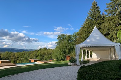 Tentes blanches pointues installées dans un jardin paysager avec vue sur une vallée boisée sous un ciel partiellement…