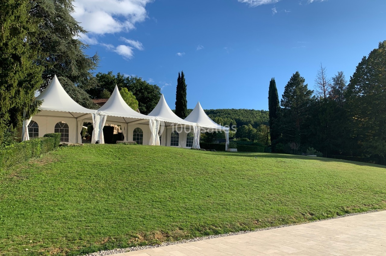 Tentes blanches installées sur une pelouse verdoyante, entourées d'arbres et sous un ciel bleu dégagé.