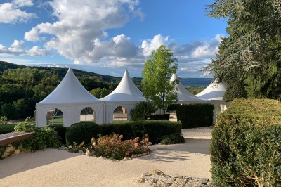 Tentes blanches pointues installées dans un jardin paysager avec vue sur une vallée boisée sous un ciel partiellement…