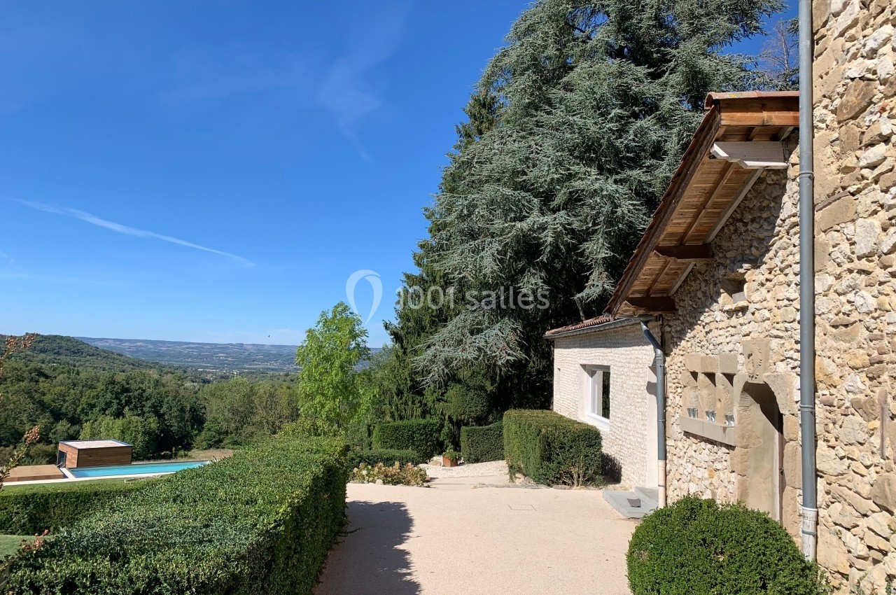 Maison en pierre avec jardin, piscine et vue dégagée sur une vallée sous un ciel bleu.