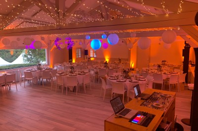 Salle de réception décorée avec des guirlandes lumineuses, des lampions suspendus et des tables dressées pour un événement.
