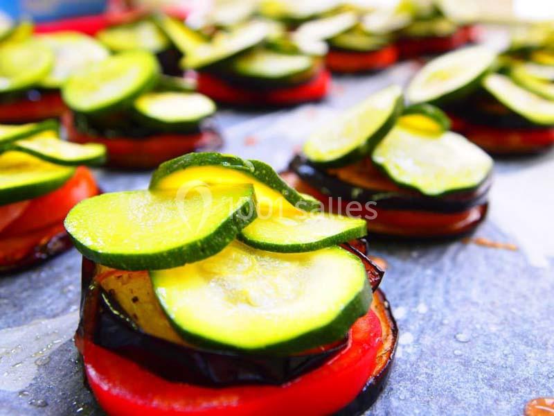 Tranches de courgettes, aubergines et tomates disposées en couches sur une plaque de cuisson.