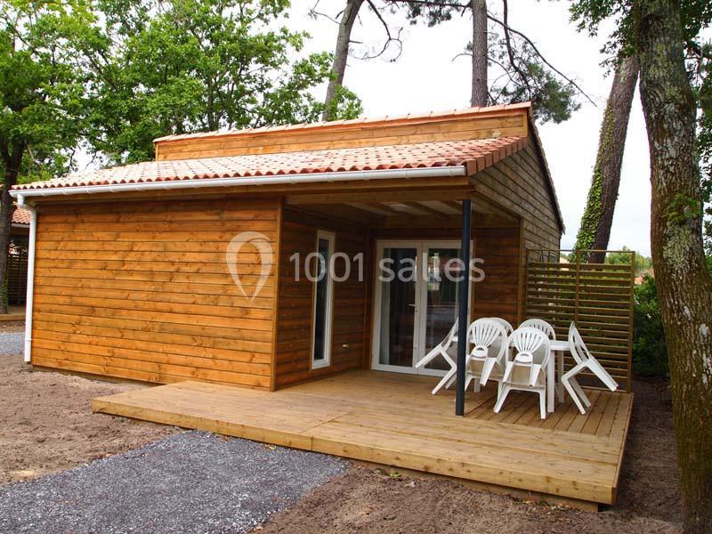 Chalet en bois avec terrasse aménagée, table et chaises blanches, entouré d'arbres dans un environnement naturel.