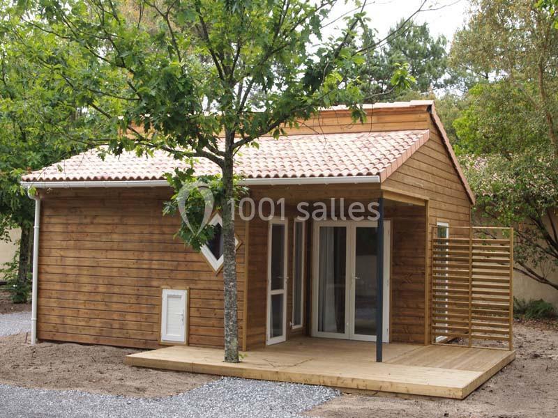 Maison en bois avec terrasse couverte, entourée d'arbres et située sur un terrain partiellement gravillonné.