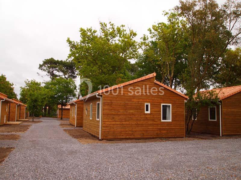 Des chalets en bois alignés dans un cadre arboré, avec des allées en gravier sous un ciel nuageux.