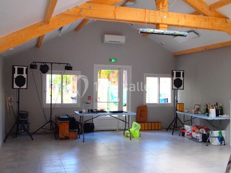 Salle lumineuse avec charpente en bois, équipée de matériel audio, tables avec boissons et objets divers.