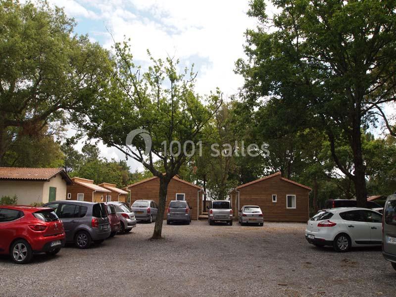 Parking avec plusieurs voitures stationnées devant des chalets en bois entourés d'arbres.