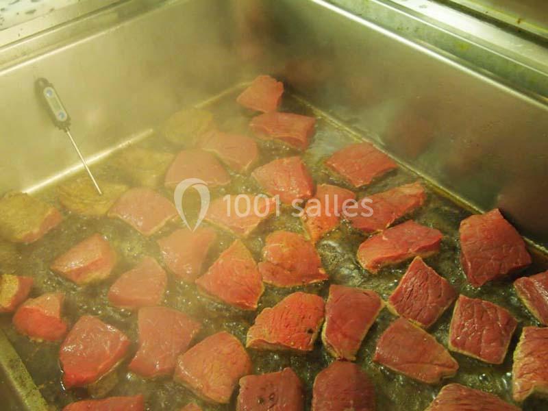 Morceaux de viande rouge en train de cuire dans une grande poêle métallique avec de la vapeur visible.