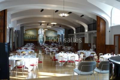 Banc en pierre au premier plan dans une allée bordée d'arbres, avec des promeneurs visibles au loin.