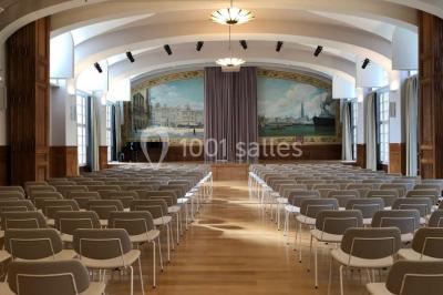 Banc en pierre au premier plan dans une allée bordée d'arbres, avec des promeneurs visibles au loin.