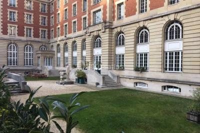 Banc en pierre au premier plan dans une allée bordée d'arbres, avec des promeneurs visibles au loin.
