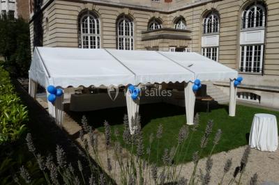 Banc en pierre au premier plan dans une allée bordée d'arbres, avec des promeneurs visibles au loin.