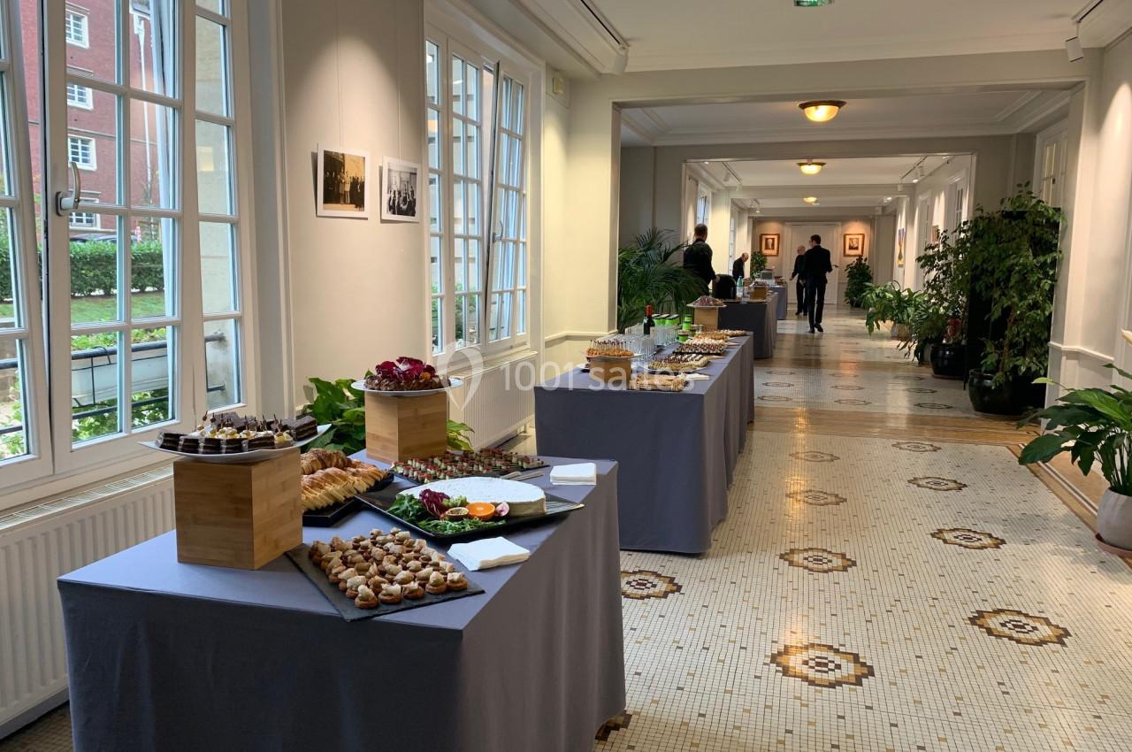 Tables dressées avec des buffets de nourriture dans un couloir lumineux, décoré de plantes et de carrelage ancien.