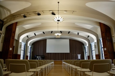 Écran de projection blanc dans une petite salle équipée de fauteuils marron et de haut-parleurs muraux.