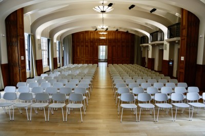 Écran de projection blanc dans une petite salle équipée de fauteuils marron et de haut-parleurs muraux.