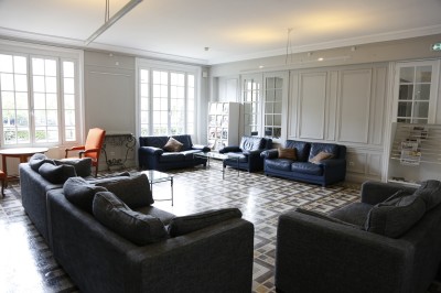 Écran de projection blanc dans une petite salle équipée de fauteuils marron et de haut-parleurs muraux.