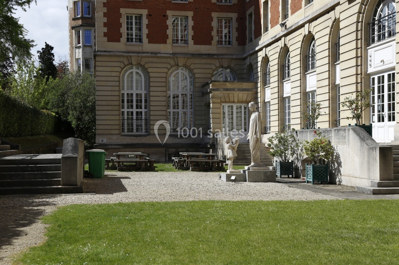 Cour intérieure avec pelouse, tables de pique-nique, statues et façade en briques et pierre avec grandes fenêtres.