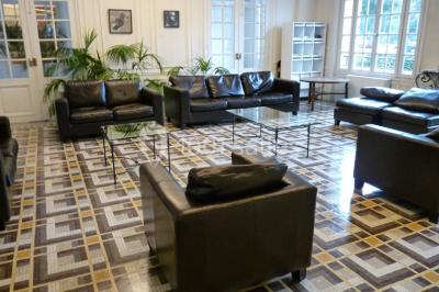 Banc en pierre au premier plan dans une allée bordée d'arbres, avec des promeneurs visibles au loin.