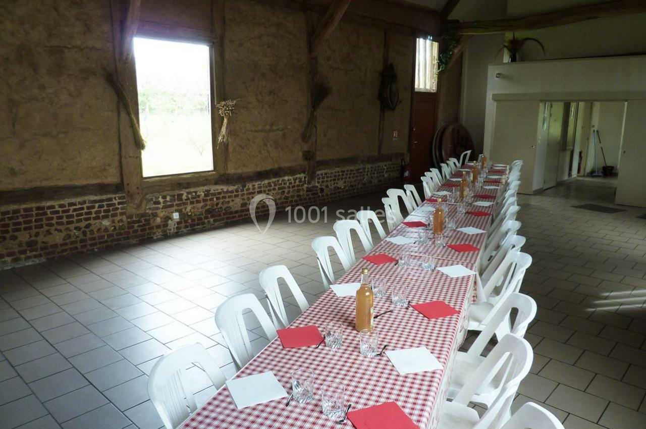 Location salle Montivilliers (Seine-Maritime) - Ferme d'Epaville #12 Grande table rectangulaire avec nappes à carreaux rouges et blancs, entourée de chaises blanches dans une salle rustique.