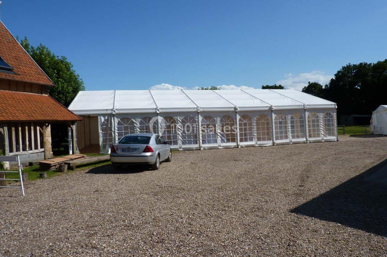 Location salle Montivilliers (Seine-Maritime) - Ferme d'Epaville #26 Grande tente blanche installée sur un terrain gravillonné, avec une voiture stationnée à proximité.