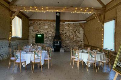 Miniature Location salle Montivilliers (Seine-Maritime) - Ferme d'Epaville #6 Salle rustique avec murs en pierre et poutres apparentes, aménagée avec tables hautes, canapés et décorations simples.