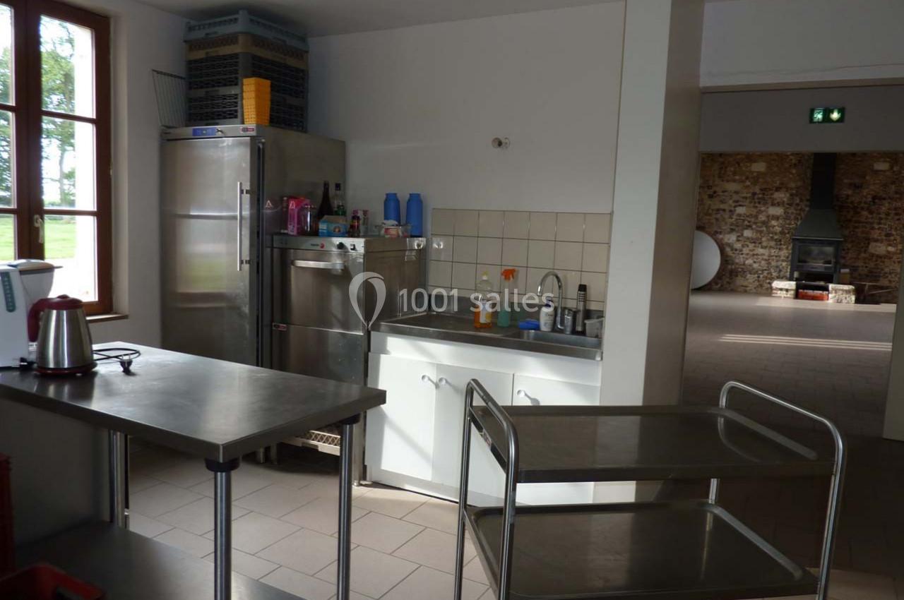 Location salle Montivilliers (Seine-Maritime) - Ferme d'Epaville #29 Cuisine professionnelle avec évier, plans de travail en inox, étagères et chariot, éclairée par une fenêtre.