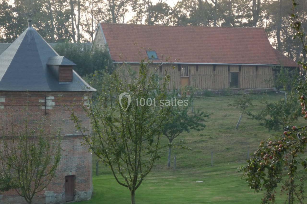 Location salle Montivilliers (Seine-Maritime) - Ferme d'Epaville #33 Bâtiments en briques et en bois dans un paysage rural avec arbres et pelouse au premier plan.