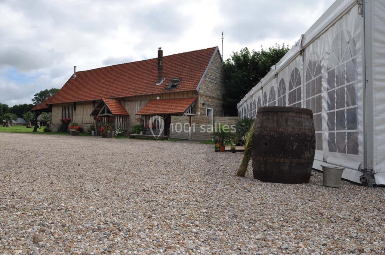 Location salle Montivilliers (Seine-Maritime) - Ferme d'Epaville #25 Maison en pierre avec toit en tuiles rouges, à côté d'une tente blanche et d'un tonneau sur une cour en gravier.