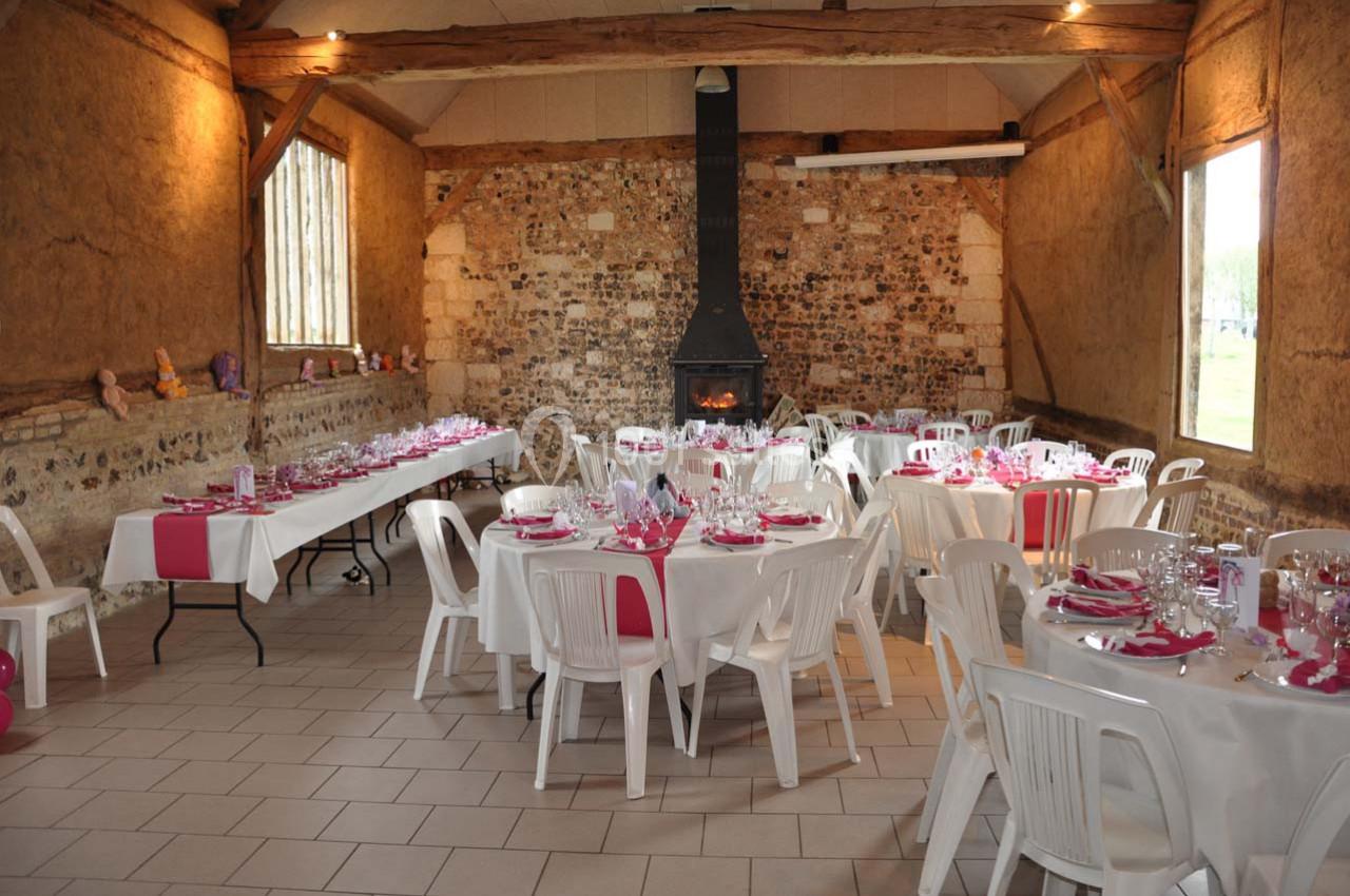 Location salle Montivilliers (Seine-Maritime) - Ferme d'Epaville #32 Salle rustique décorée pour un événement, avec tables dressées, nappes blanches et accents roses, cheminée au fond.