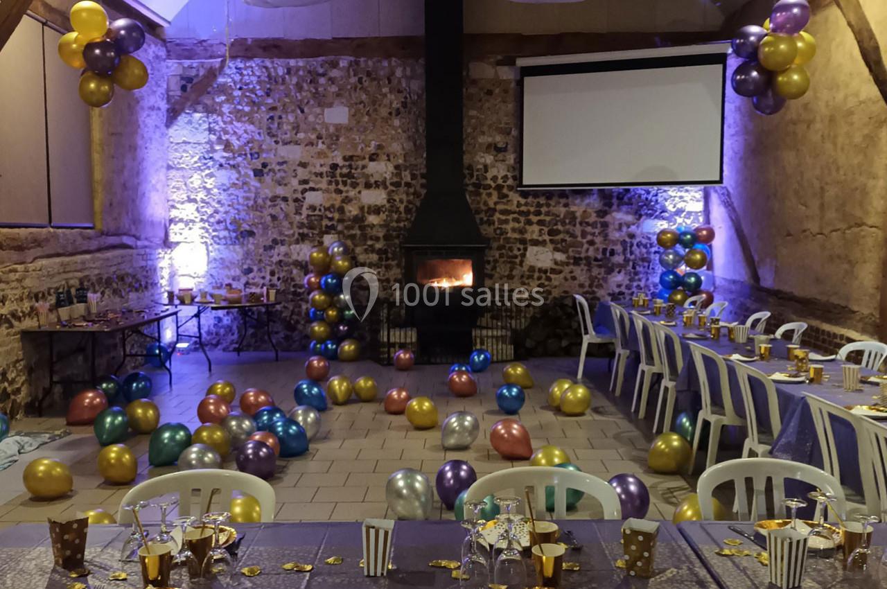 Location salle Montivilliers (Seine-Maritime) - Ferme d'Epaville #28 Salle décorée pour une fête avec des ballons colorés, un poêle allumé et des tables dressées avec vaisselle festive.