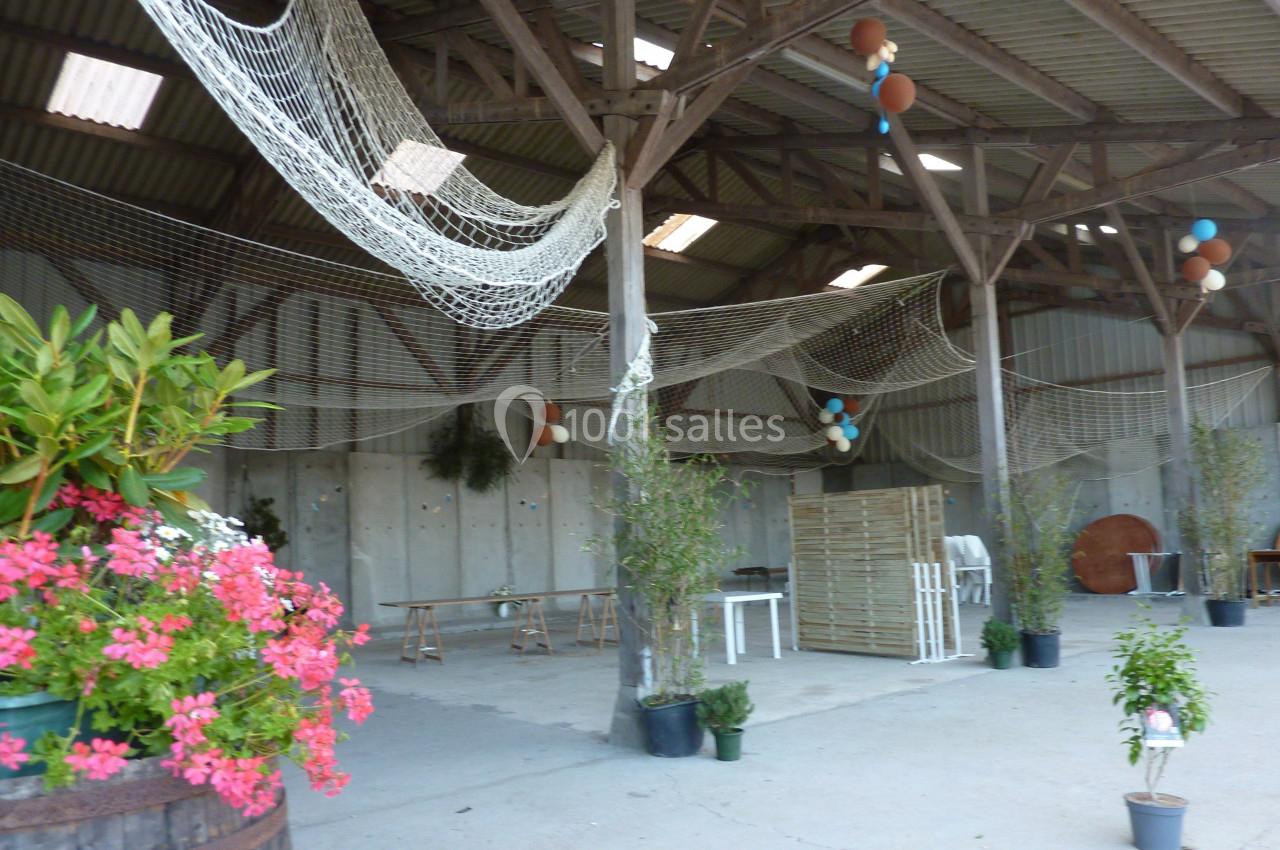 Location salle Montivilliers (Seine-Maritime) - Ferme d'Epaville #36 Intérieur d'une grange décorée avec des filets suspendus, des plantes en pot et des tables en bois.