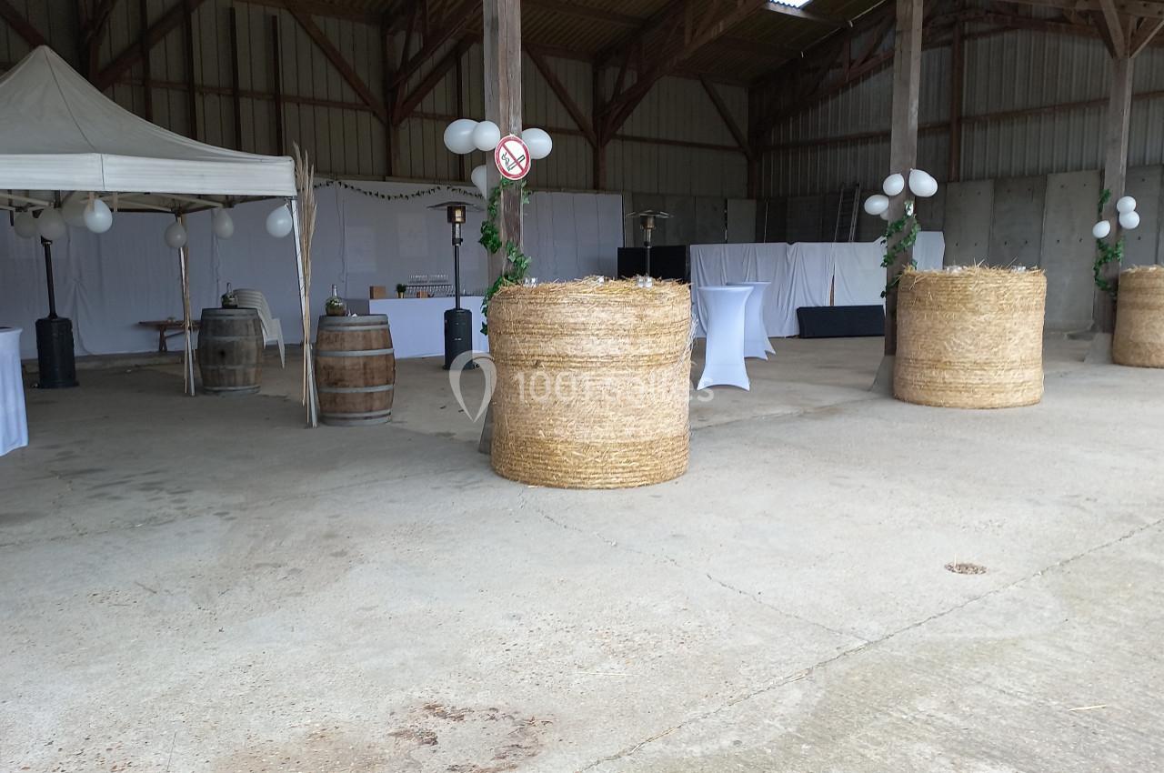 Location salle Montivilliers (Seine-Maritime) - Ferme d'Epaville #37 Espace de réception dans une grange avec tables hautes, bottes de paille décorées et tente blanche.