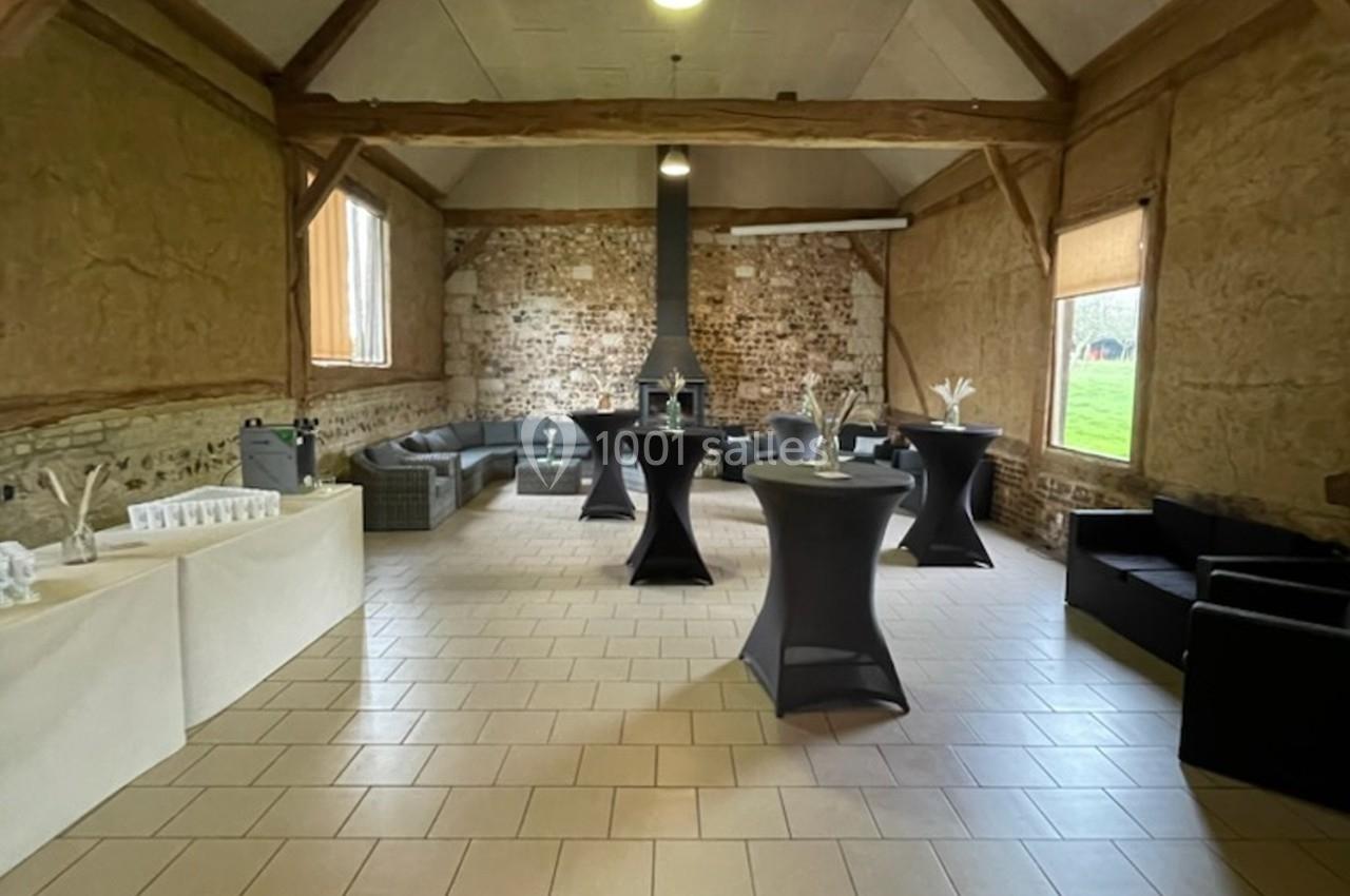 Location salle Montivilliers (Seine-Maritime) - Ferme d'Epaville #40 Salle rustique avec murs en pierre et poutres apparentes, aménagée avec tables hautes, canapés et décorations simples.