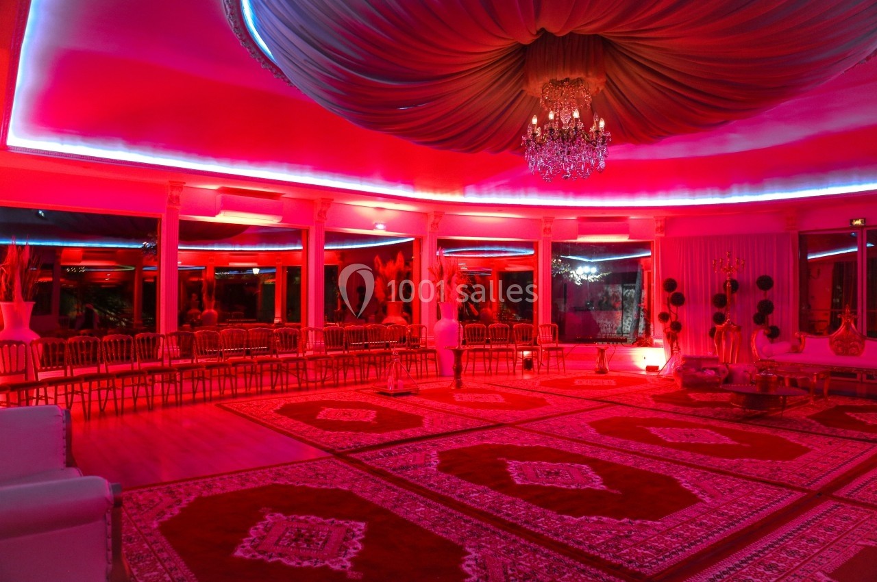 Salle de réception circulaire éclairée de lumières rouges, avec tapis orientaux et chaises disposées en périphérie.