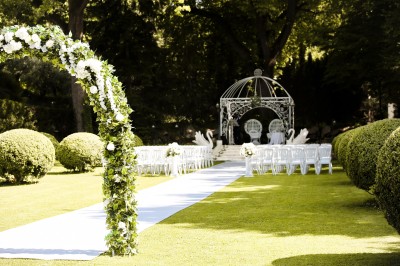 Cérémonie de mariage en plein air avec des invités assis, un couple avançant vers une arche décorée.