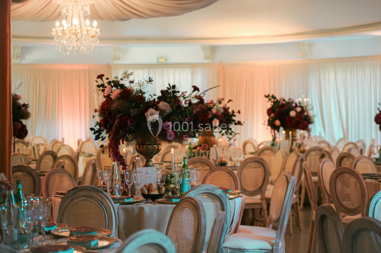 Salle de réception élégante avec tables décorées de fleurs et chaises en bois clair sous un éclairage chaleureux.